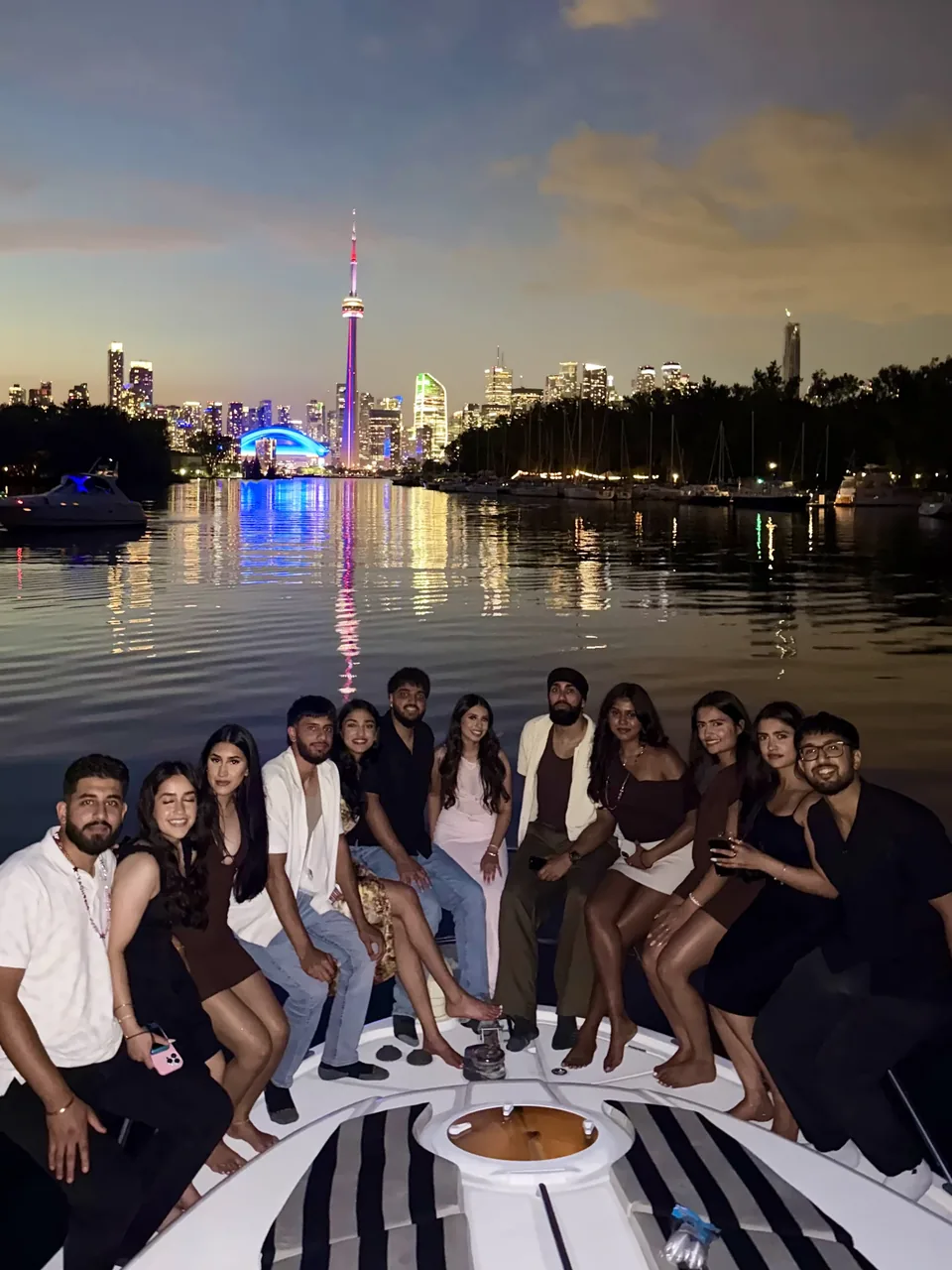 A full party on the bow at night, the CN Tower lit behind them.
